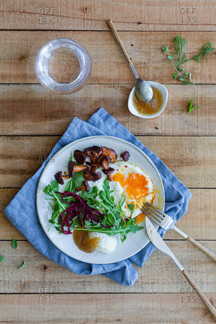 Top view of plate with palatable fried egg served with mushrooms and fresh salad on wooden table with sauce and glass of water