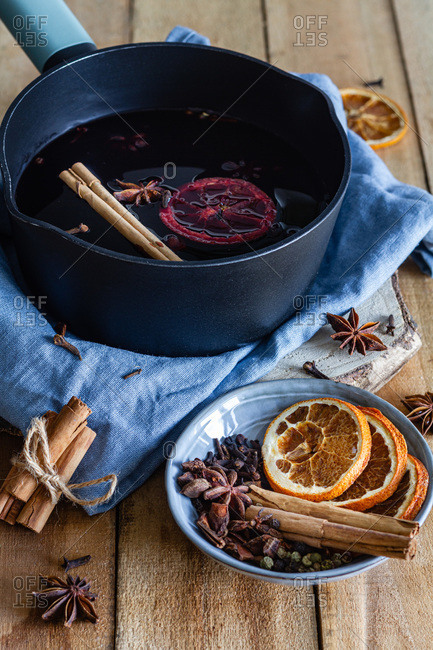 High angle of saucepan with hot tasty mulled wine with cinnamon stick and dried oranges arranged on table with star anise and dry cloves in kitchen