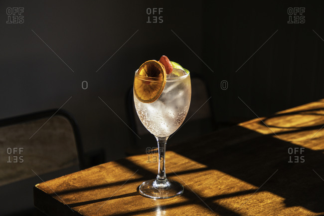 Crystal goblet with cold alcohol cocktail with ice and sliced orange placed on wooden table in bar