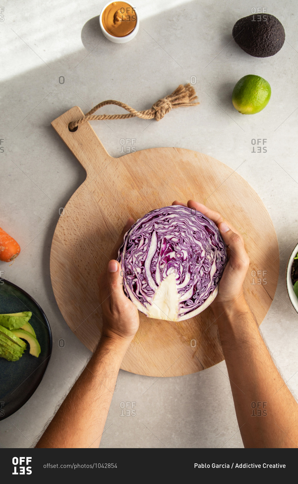 Top view of crop anonymous person placing halved fresh red cabbage on wooden cutting board while preparing delicious salad in kitchen