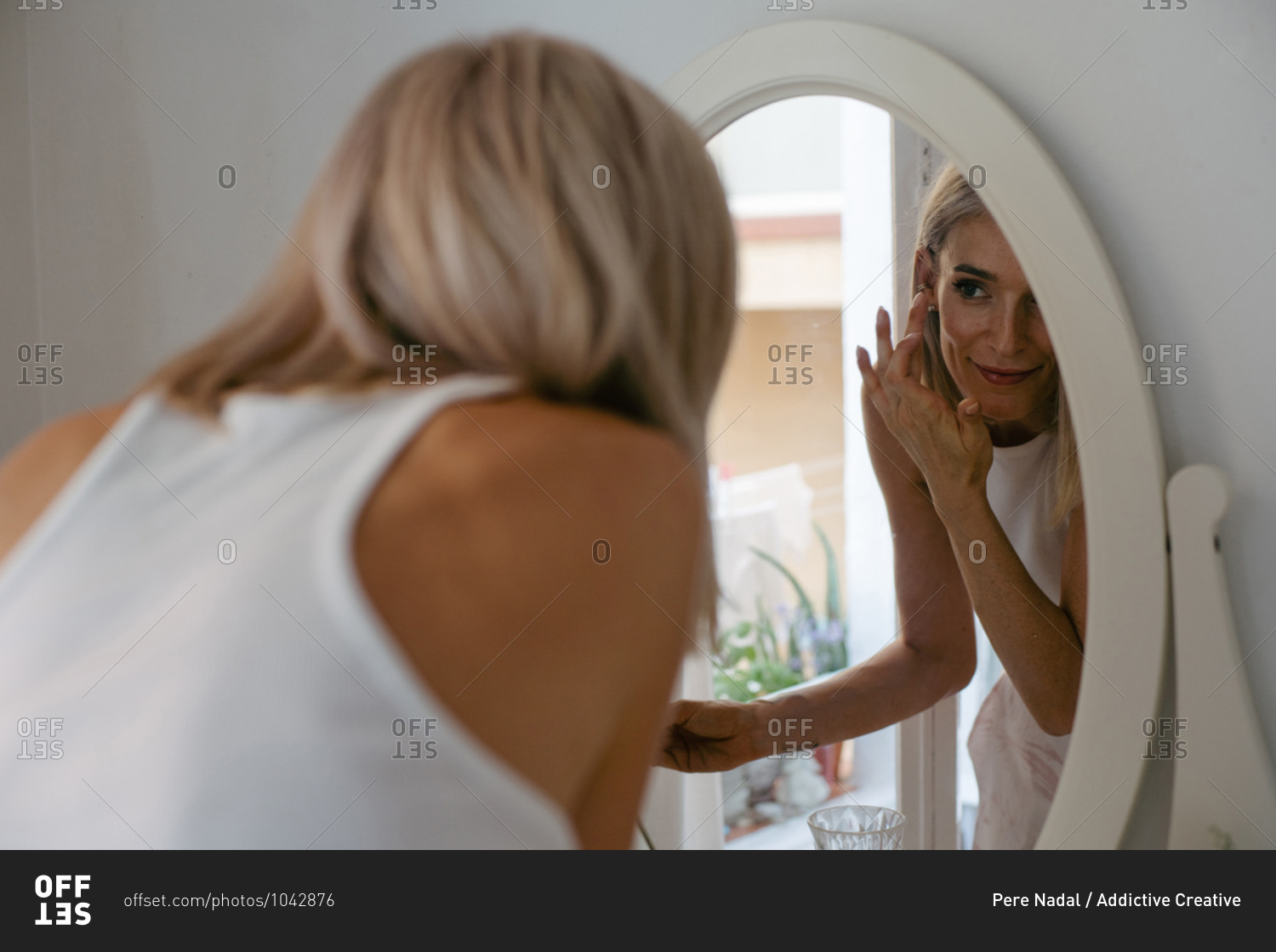 Charming female applying lip pencil and doing makeup at home while reflecting in mirror