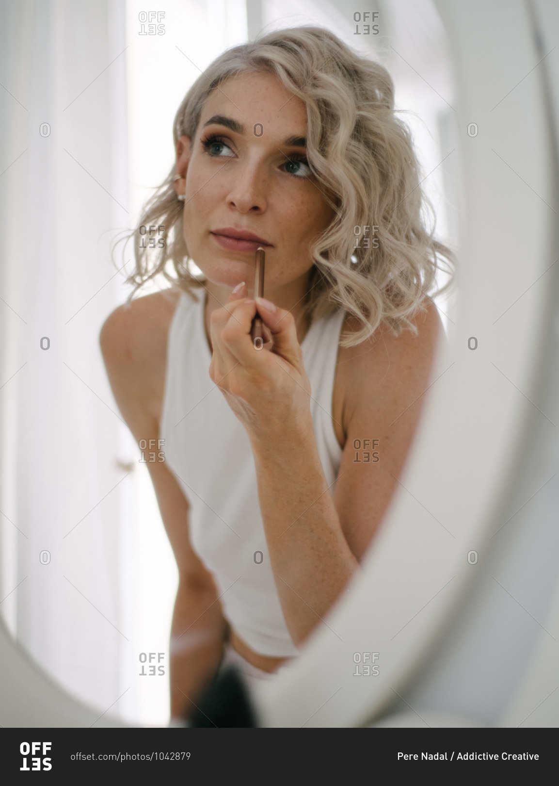Low angle of charming female applying lip pencil and doing makeup at home while reflecting in mirror