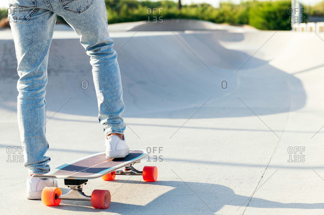 Unrecognizable stylish skater in jeans and sneakers standing on skateboard in skatepark on sunny day in summer