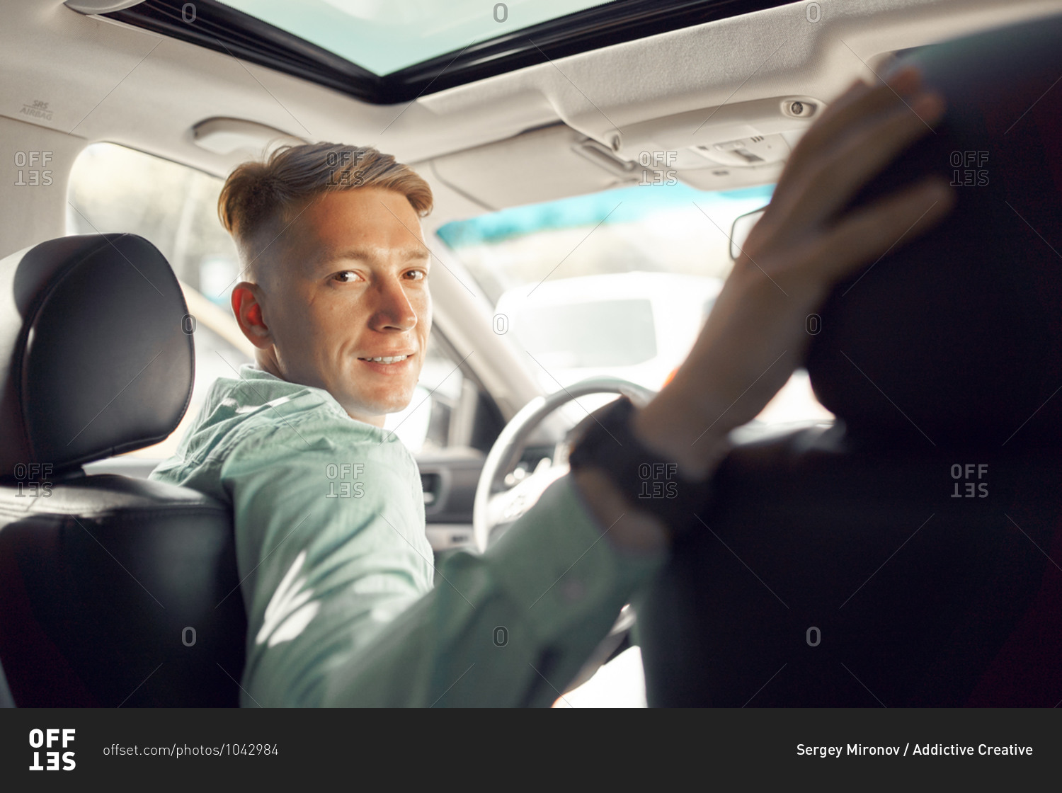 Side view of handsome smiling male driver sitting in parked luxury car and looking at camera