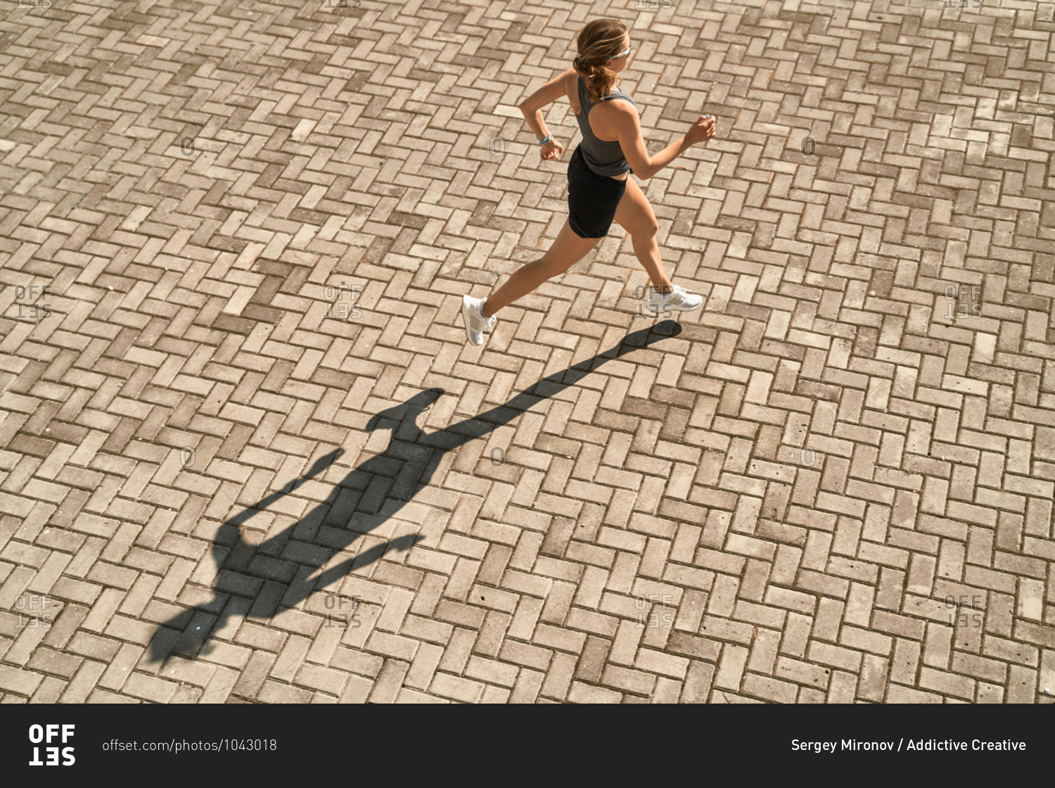 From above full body of active slim female in sportswear running fast on paved square in sunny day