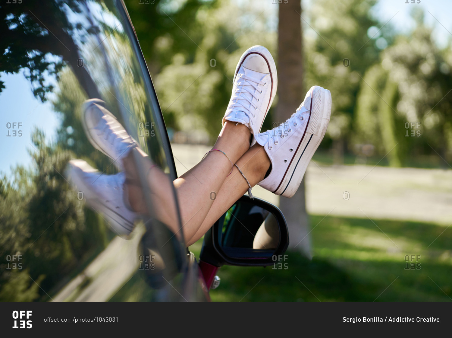Unrecognizable crop female resting in parked car with legs out of window on sunny day in summer