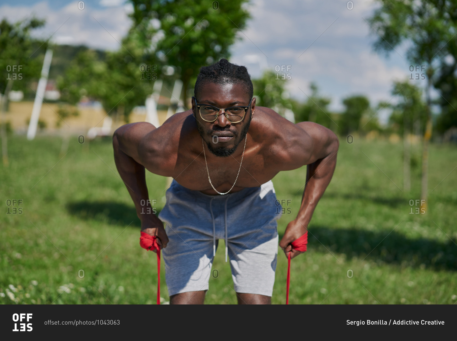 Strong active African American male with naked muscular torso doing resistance bend bicep curl exercise during functional workout on street