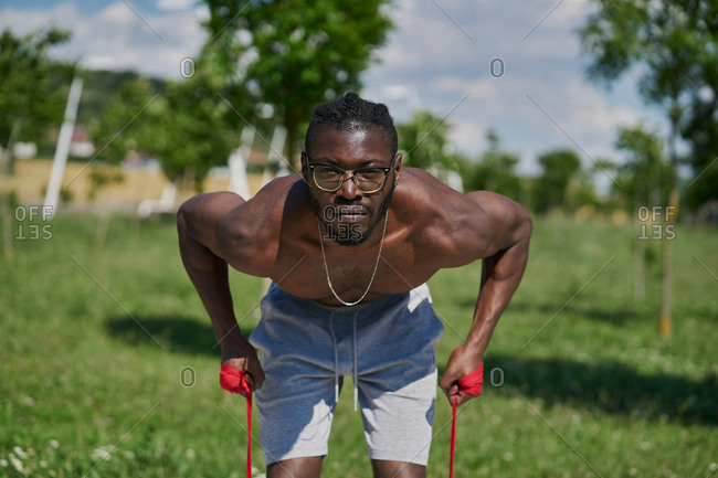 Strong active African American male with naked muscular torso doing resistance bend bicep curl exercise during functional workout on street