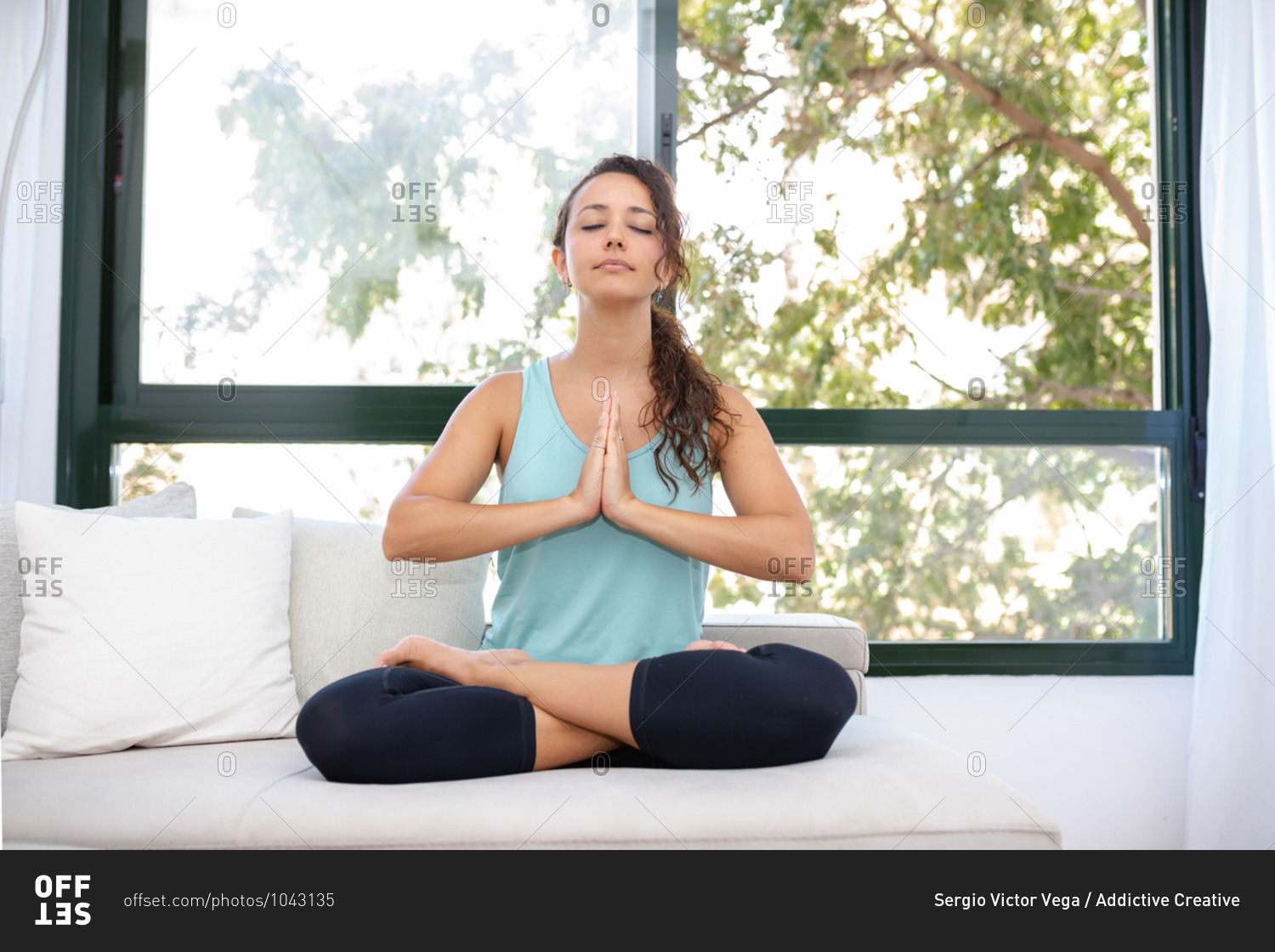 Concentrated flexible female sitting with crossed legs doing yoga in Padmasana while practicing mindfulness with closed eyes