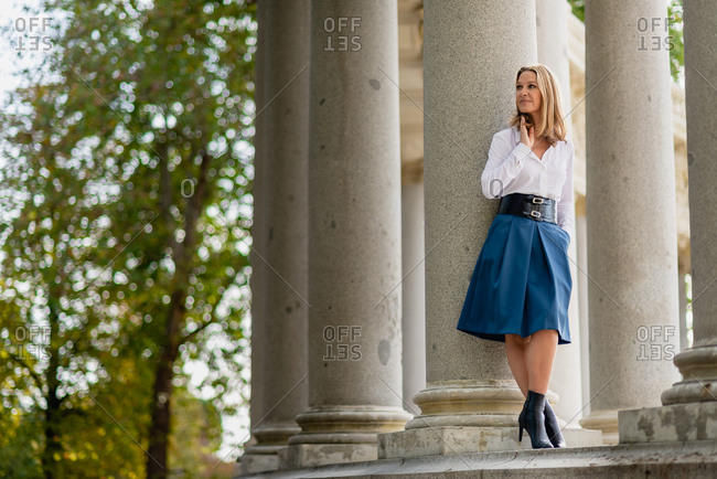 Tender female in elegant skirt standing near stone column in park in summer and looking away