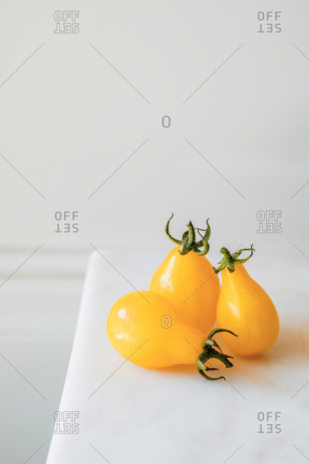 High angle of whole and cut ripe yellow tomatoes placed on white table with fresh green herbs