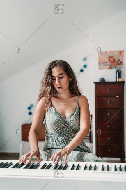 Talented ethnic female musician playing piano while sitting in modern apartment and rehearsing