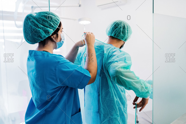 Back view of vet doctors putting on protective uniform and gloves while standing in bright operating theater of veterinarian hospital and preparing for surgery