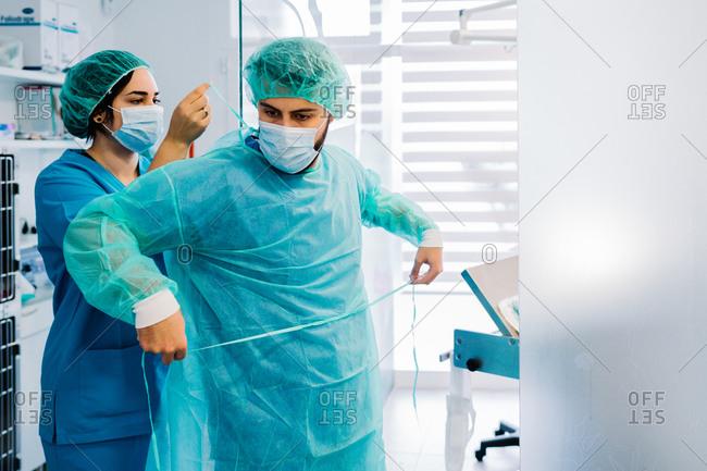 Side view of vet doctors putting on protective uniform and gloves while standing in bright operating theater of veterinarian hospital and preparing for surgery