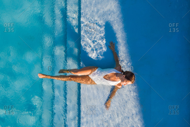 Aerial view of woman laying on the stairs of a swimming pool in a white swimsuit.
