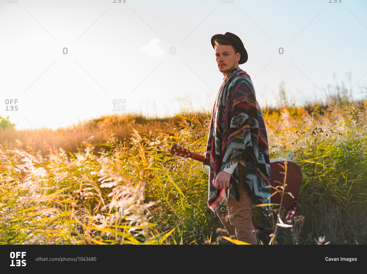 Folk musician with acoustic guitar posing in poncho in rural area