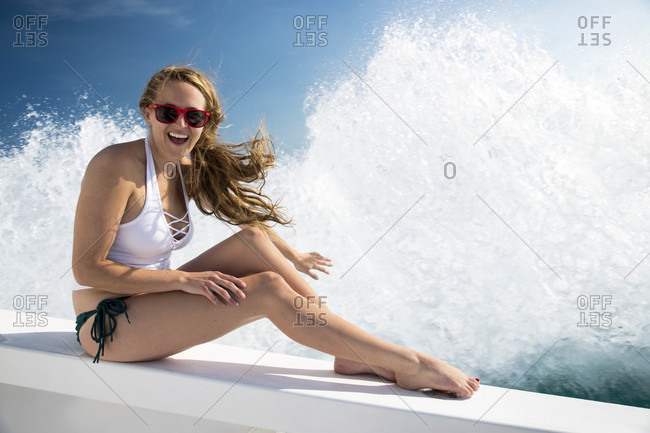 Cheerful young woman sitting on boat while waves splashing in background