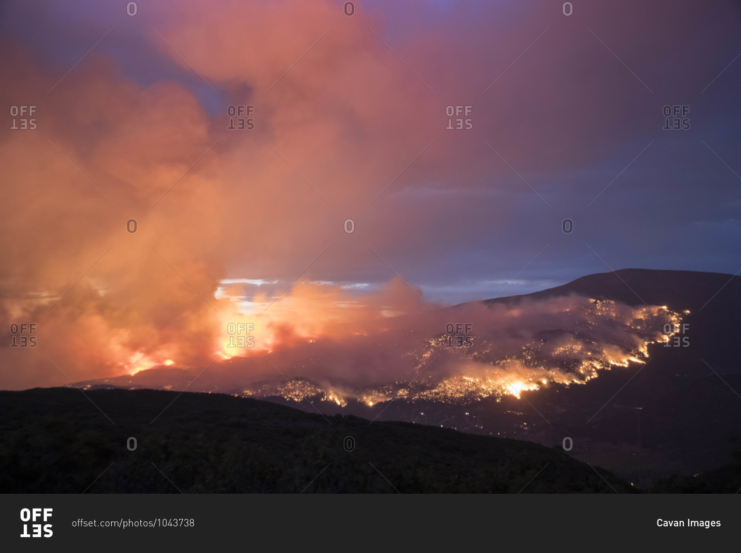 Smoke emitting from wildfire on mountain against sky at dusk
