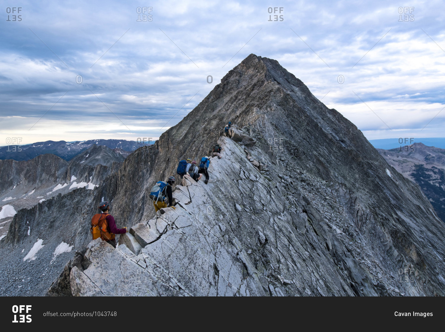 Male and female hikers climbing mountain peak against cloudy sky
