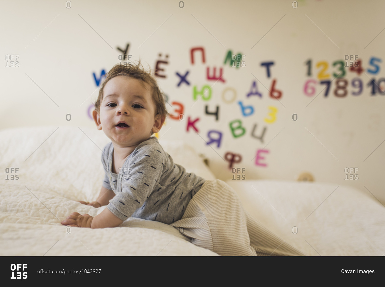 Baby crawling on white bedspread with letters and numbers on wall
