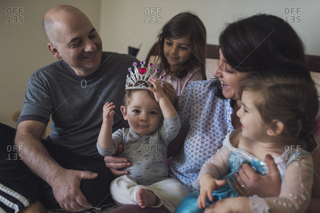 Entire family in parent's bed laughing at 1 yr old baby wearing tiara