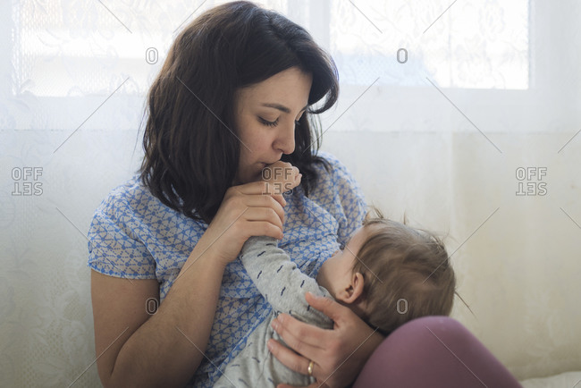 Tender loving mother kissing hand of baby while breastfeeding
