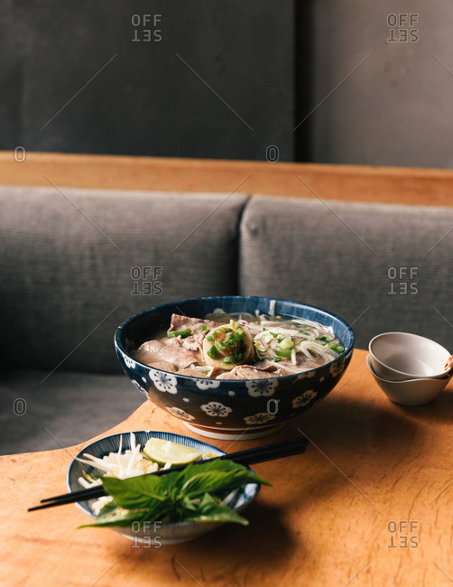 A bowl of traditional Vietnamese bone marrow Pho with sides on table