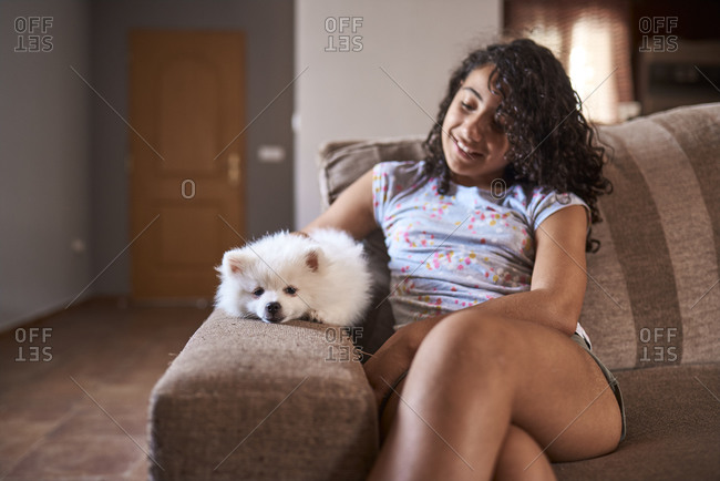 A puppy rests next to its owner on the armrest of the sofa