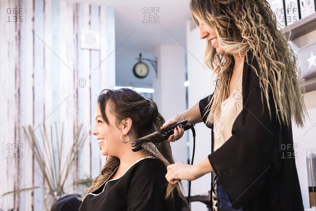 Hairstylist curling hair woman client in hairdressing beauty salon