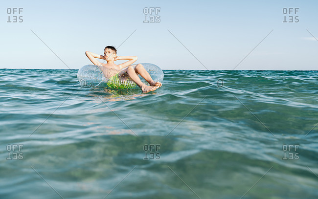 Relaxed Caucasian boy swimming in a float in the sea enjoying calm waves in summertime