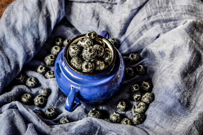 A group of blueberries in a metallic cup on a blue cloth