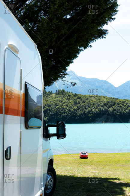 RV motorhome in front of a blue lake with mountains and a red Kayak