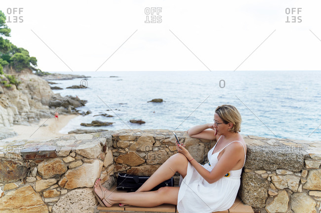 Attractive blonde woman using her smartphone on the coast during her summer vacation