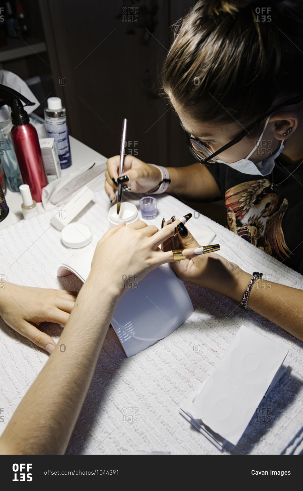 Woman in mask making French manicure to crop client during epidemic