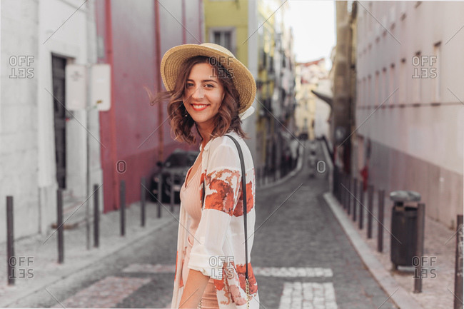 Young woman in a hat smiling and walking on a small street of Europe