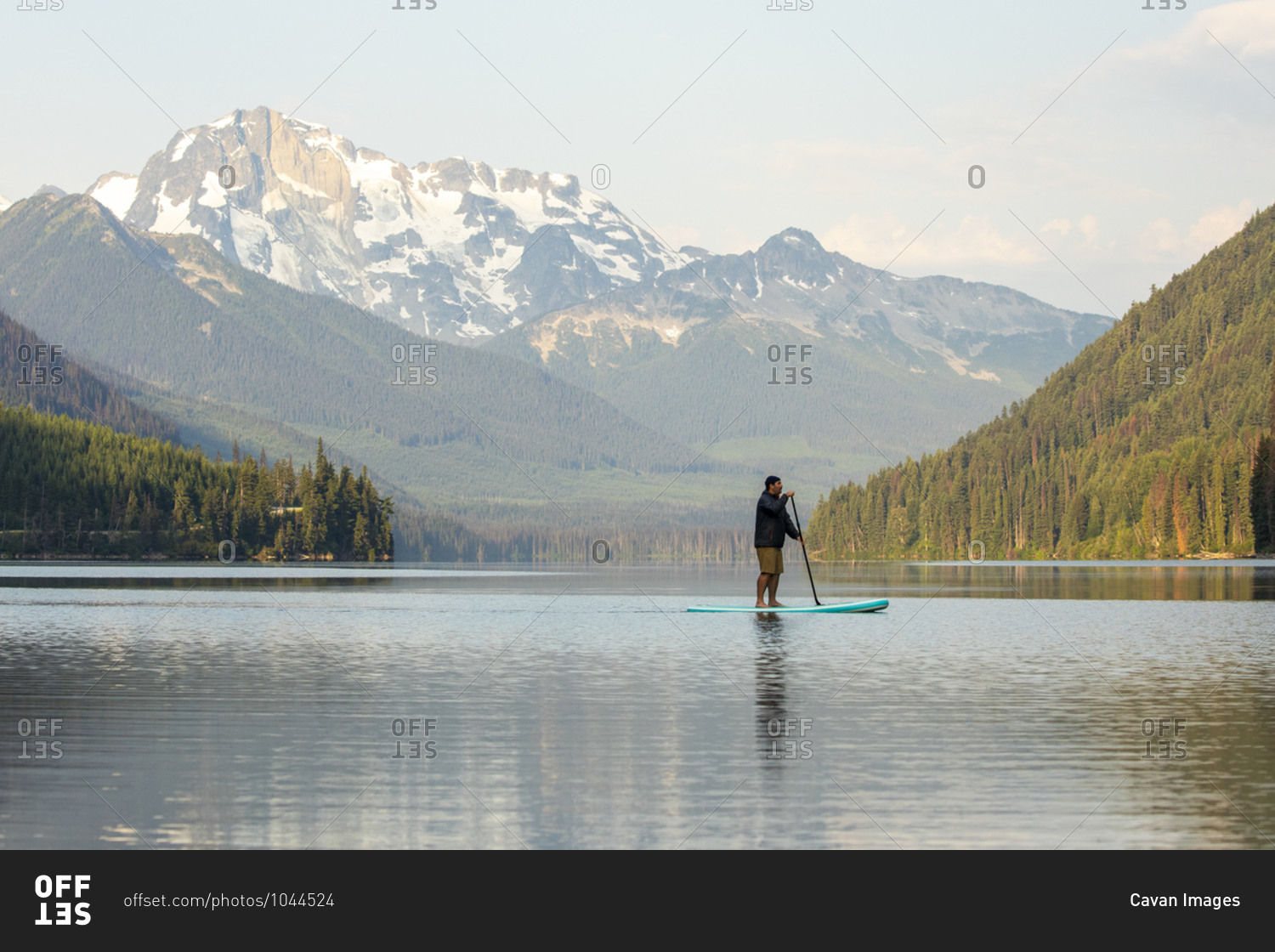 Side view of male on paddle board Duffey Lake on background of spectacular mountain ridge in morning in British Columbia