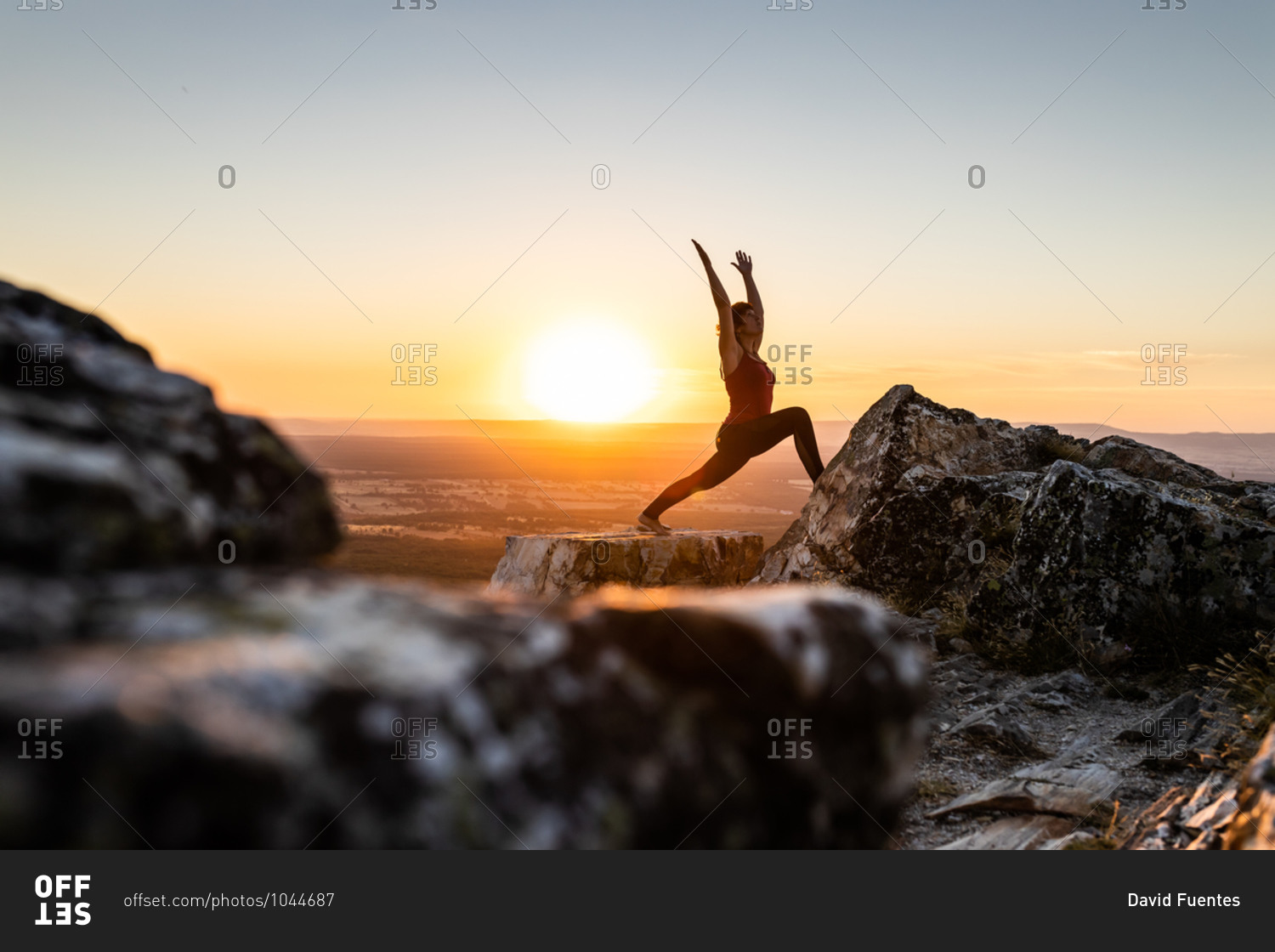 Young yogi woman practicing yoga on a rock in the mountain with the light of sunrise, side view with one leg on a rock and arms raised
