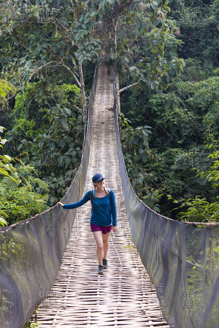 November 27, 2014: A woman crosses a precarious looking suspension bridge over the jungle in Laos, Indochina, Southeast Asia, Asia