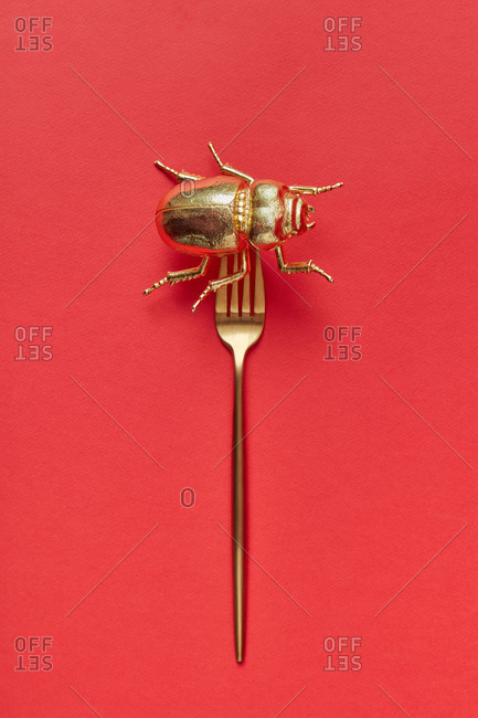 Creative set from bug made from gold metal on a golden fork on a coral background, copy space. Top view.