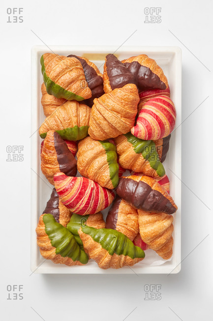Plastic container with homemade croissants in a sweet green, chocolate and jam icing on a light gray background. Top view. Continental breakfast concept.