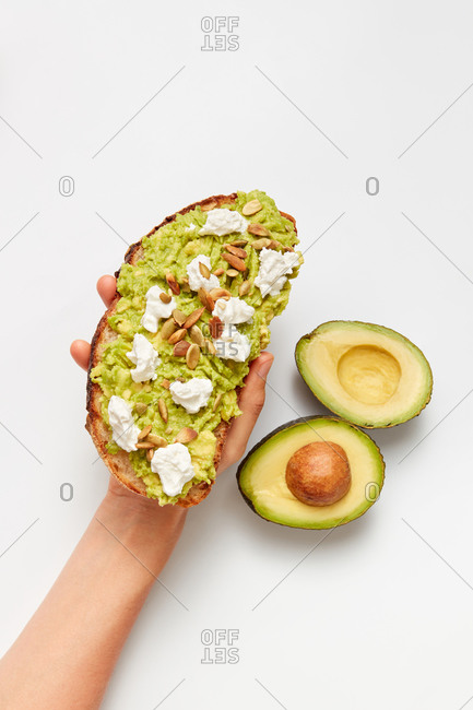 Health sandwich homemade with natural organic avocado, soft cheese, and pumpkins seeds on a woman's hand above light grey background, copy space. Top view. Healthy natural food concept.