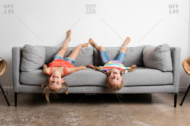 Two smiling little girls lying upside down on sofa at home stock photo -  OFFSET