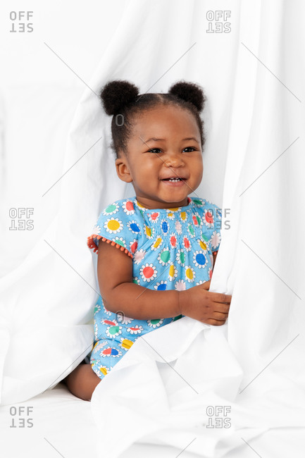 Smiling baby girl with hair buns playing behind white sheet
