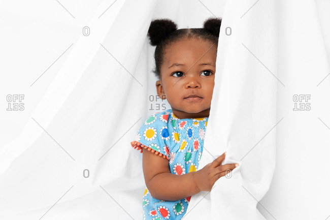 Baby girl with hair buns peeking behind white sheet
