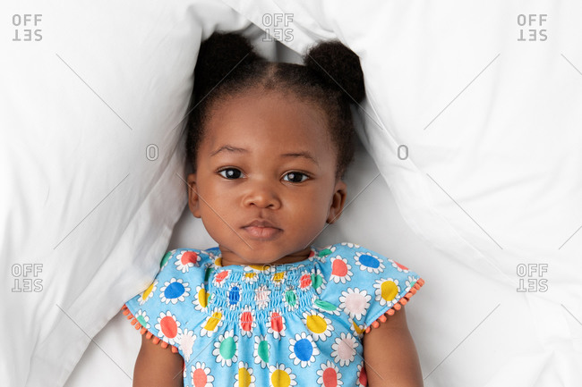 Portrait of toddler girl with hair buns lying on white bed
