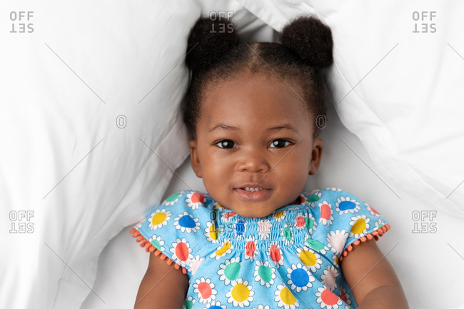 Smiling baby girl with hair buns lying on white bed