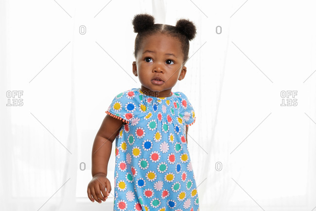 Portrait of toddler girl with hair buns in front of curtains stock photo -  OFFSET