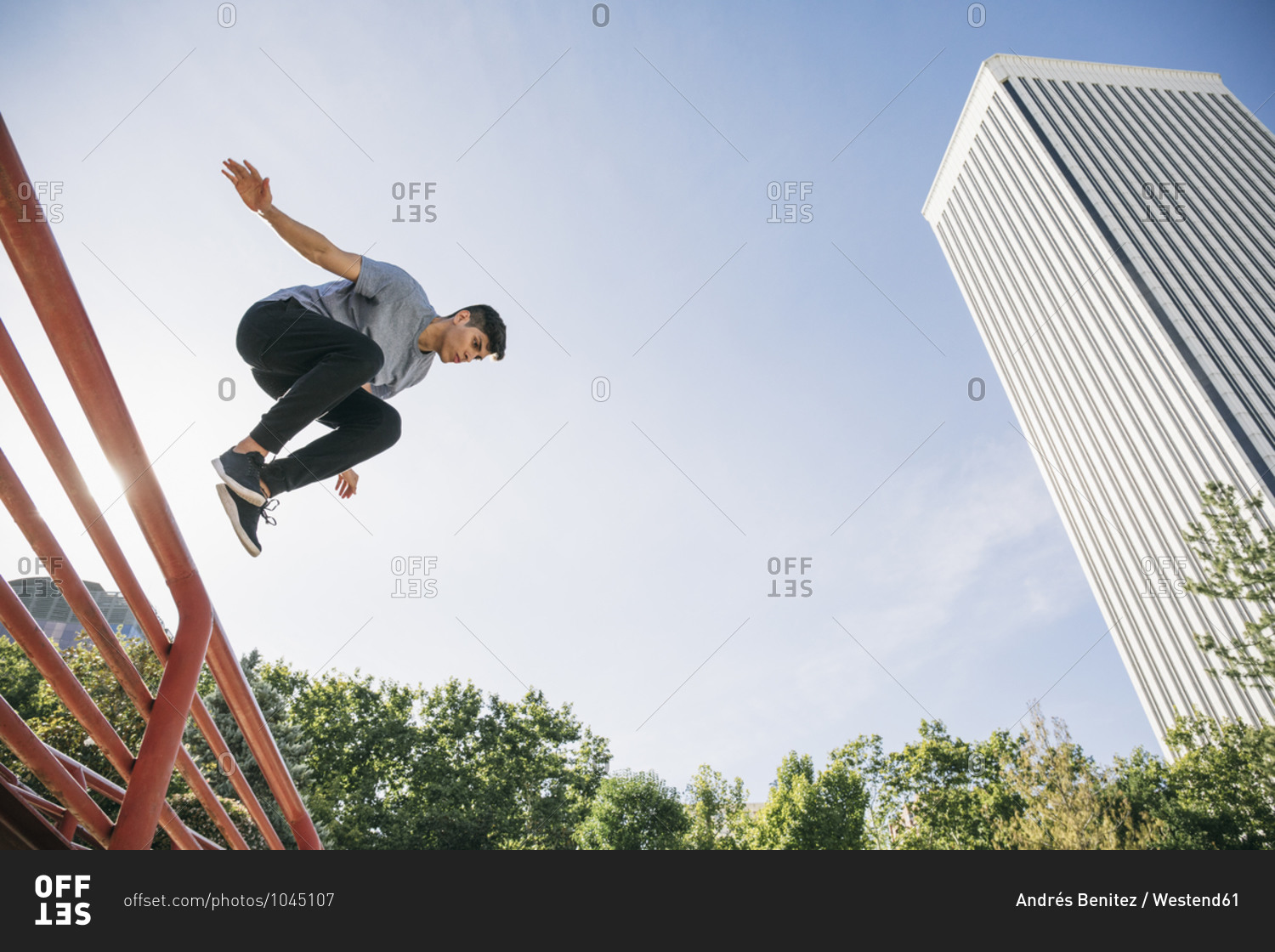 Young man performing parkour over railing against clear sky in city