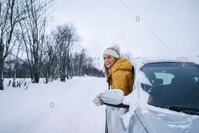 Smiling woman peeking through car window against sky during winter