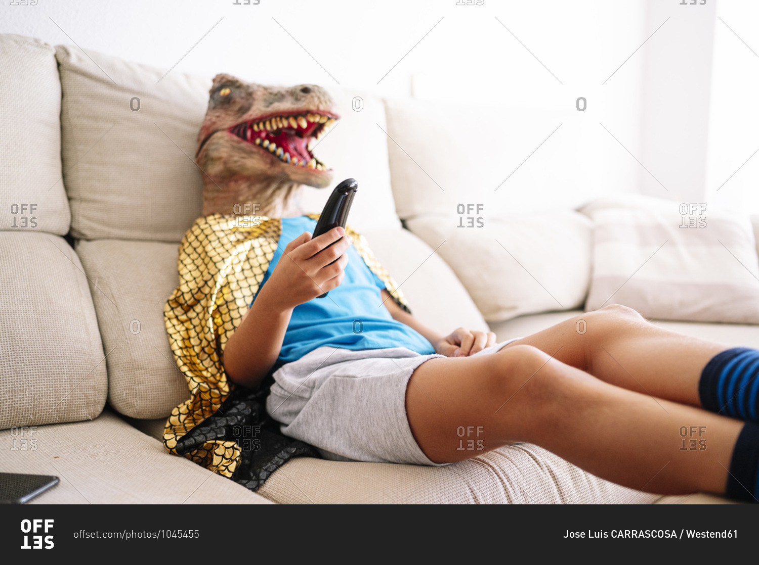 Boy wearing dinosaur mask watching TV while relaxing on sofa at home